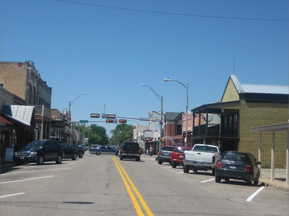 Cars parked along Bastrop's main street, two-storey brick storefronts on both sides