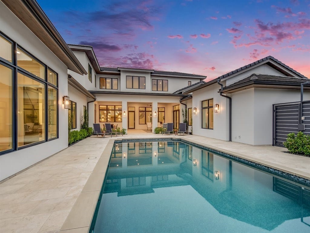 A contemporary Bee Cave house at dusk, warm light in tall windows above a rectangular pool