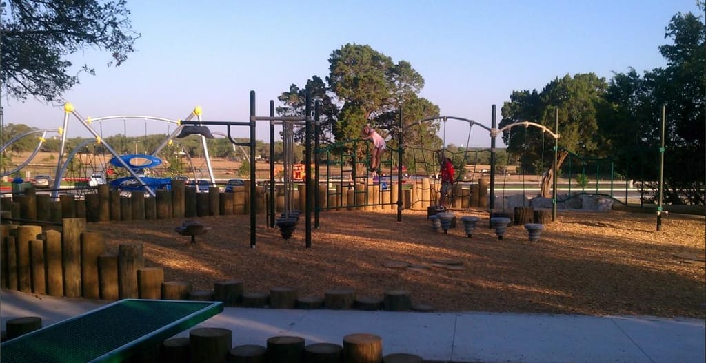Timber play structures and swings on a wood-chip playground in Cedar Park