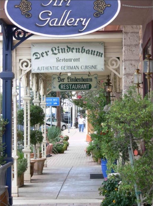 A sidewalk in Fredericksburg beneath a hanging sign for a German restaurant