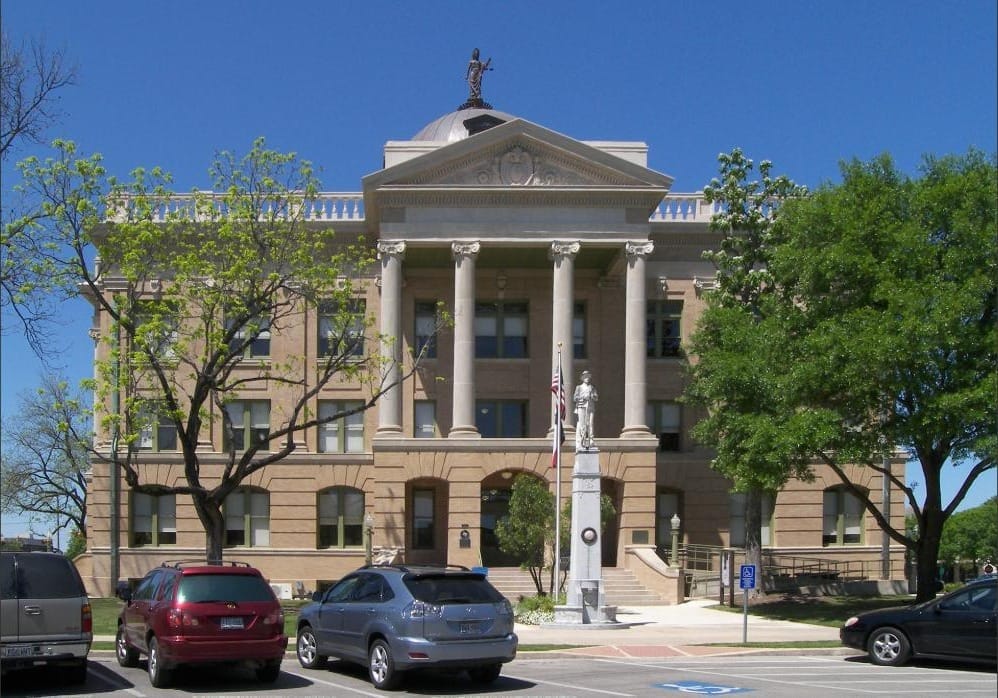 The limestone Williamson County courthouse on the Georgetown square, cars angled at the kerb