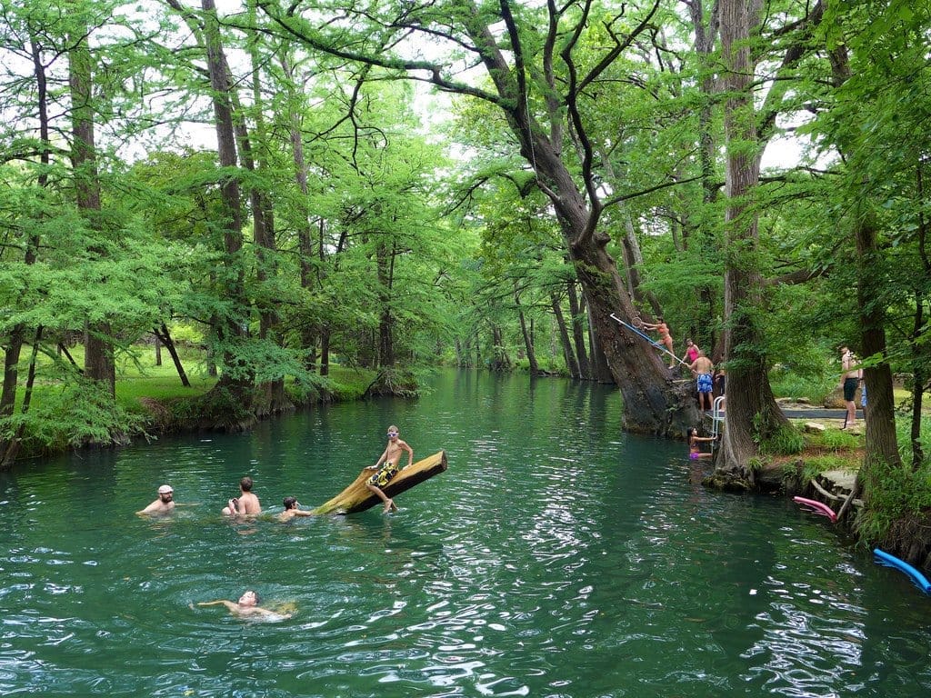 Swimmers and a diving platform at a cypress-shaded swimming hole in Wimberley