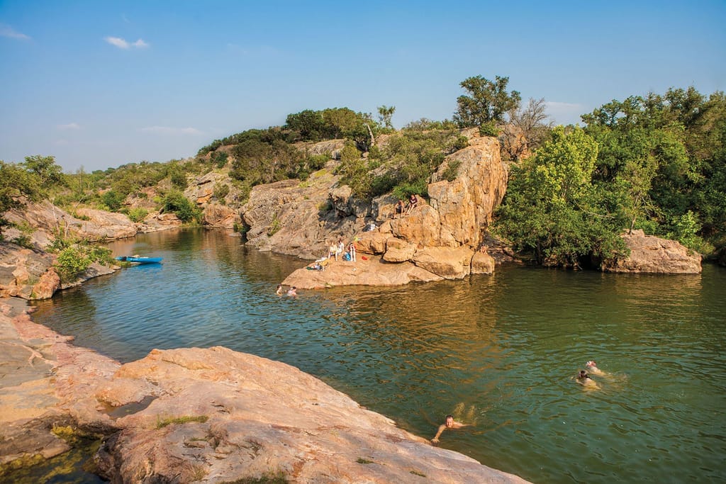 Pink granite outcrops sloping into the clear water of Inks Lake, a swimmer near the rock