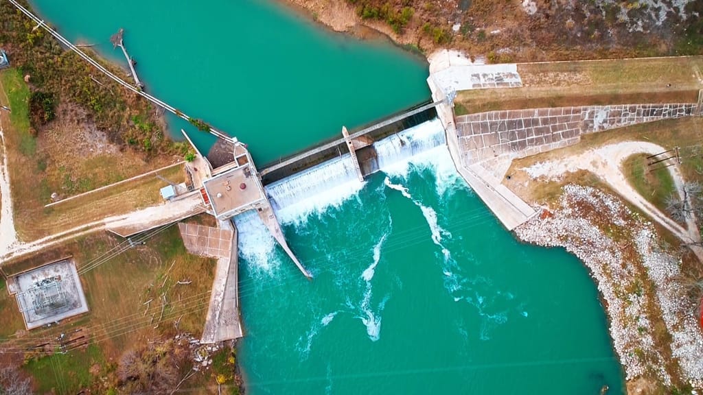 Turquoise water passing through the gates of the concrete spillway at Lake Wood