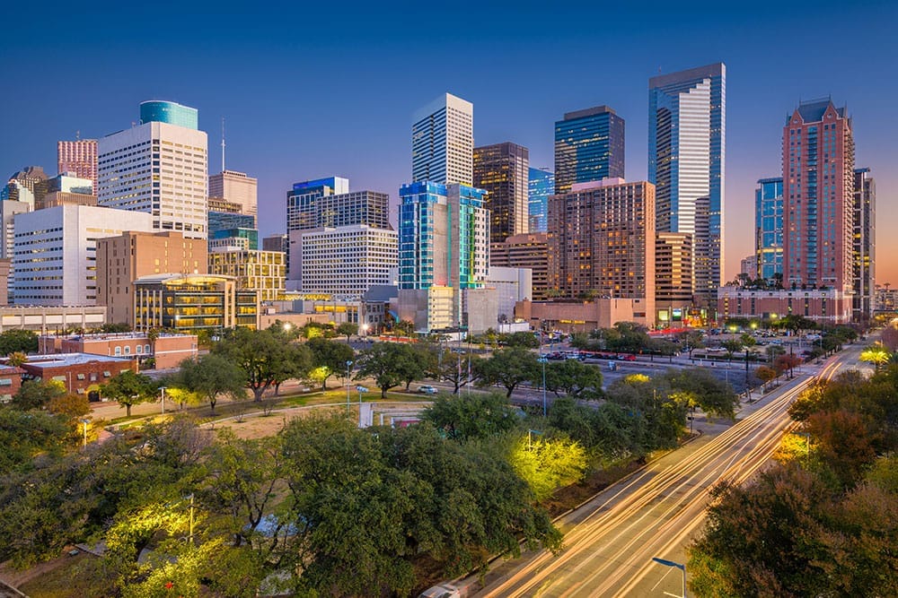 The Houston skyline at dusk, lit towers above a freeway running through the trees