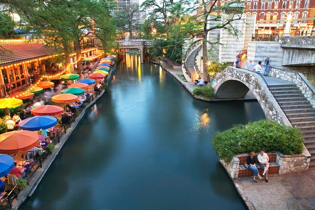The San Antonio River Walk, coloured umbrellas along the water beside a stone arch bridge