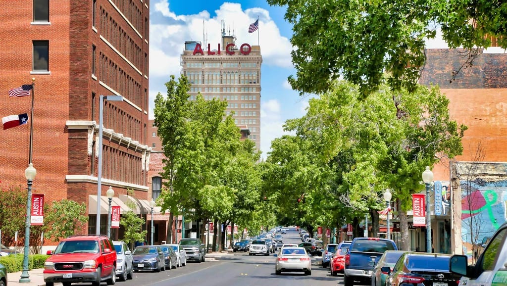 A tree-lined downtown Waco street with the ALICO building rising behind the storefronts