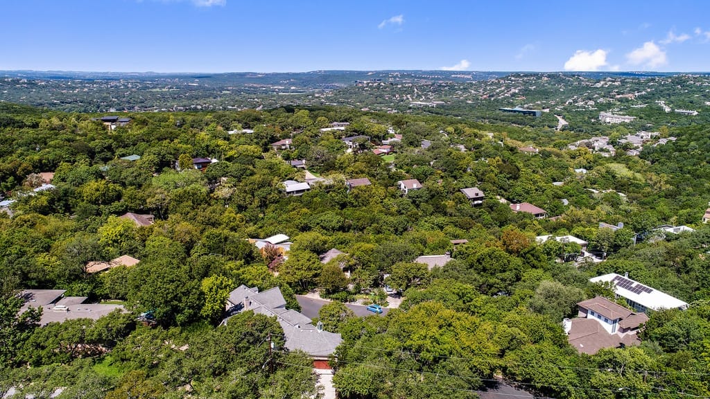 A tree-lined residential street in Central Austin, older homes set back behind deep front yards