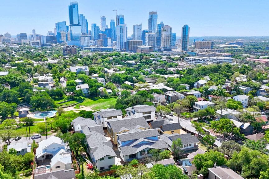 Aerial view across rooftops and a small green park toward the downtown Austin skyline on a clear day