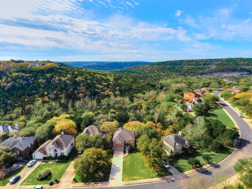 Two storey houses on a curving street in Great Hills, backing onto a wooded canyon that runs to the hills beyond