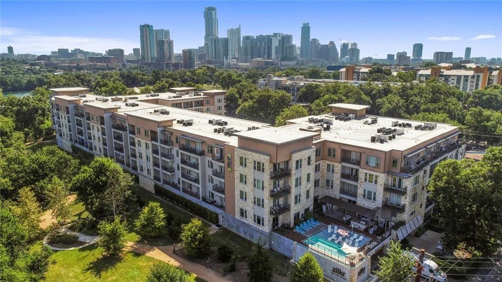 Zilkr on the Park from the air, a five storey courtyard building in stone and stucco, the downtown Austin skyline behind it