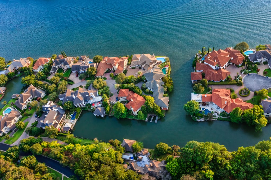 Aerial view of Lake Austin waterfront homes with tile roofs and pools on a wooded peninsula split by a narrow channel