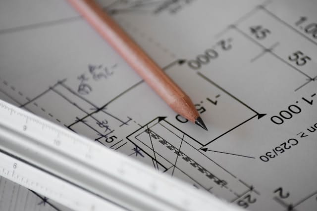 A pencil resting on a set of architectural drawings, dimensions marked along the elevation