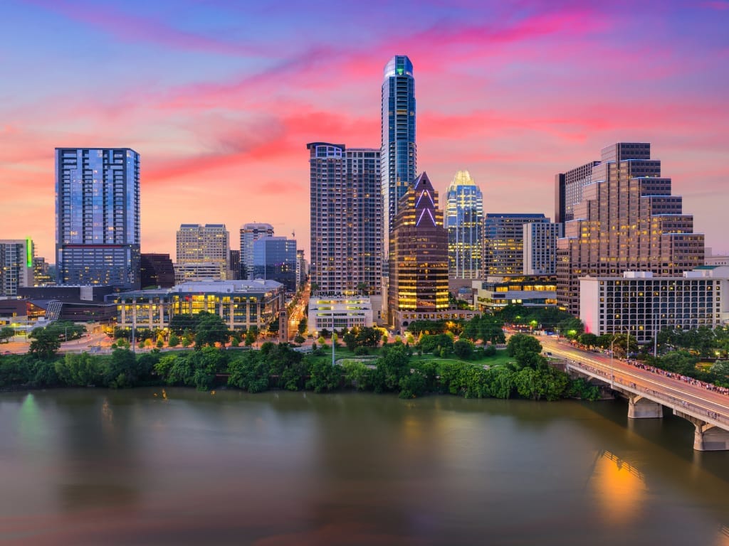 The Austin skyline at sunset, pink cloud over the towers and the whole scene reflected in the lake